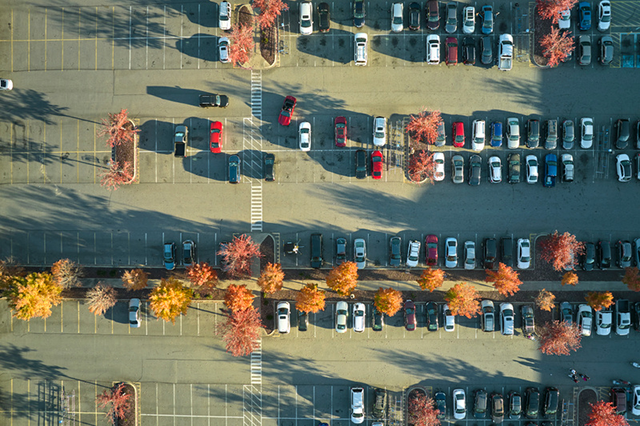 Vy uppifrån över en parkeringsplats med parkerade bilar omgivna av träd med orange höstlöv.